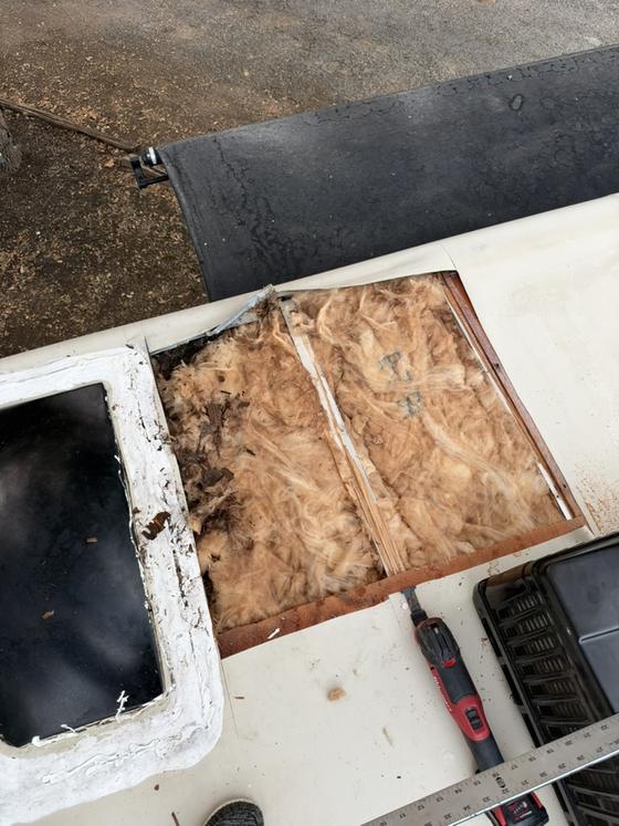 An RV roof opened up at a vent, old membrane peeled back with insulation and framing exposed