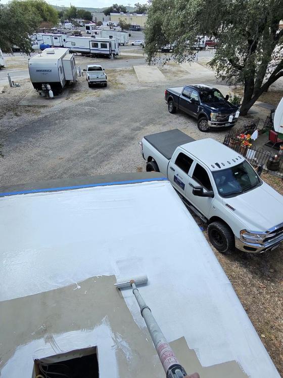 A roller applying white CrazySeal roof coating to an RV roof, showing the line between coated and uncoated